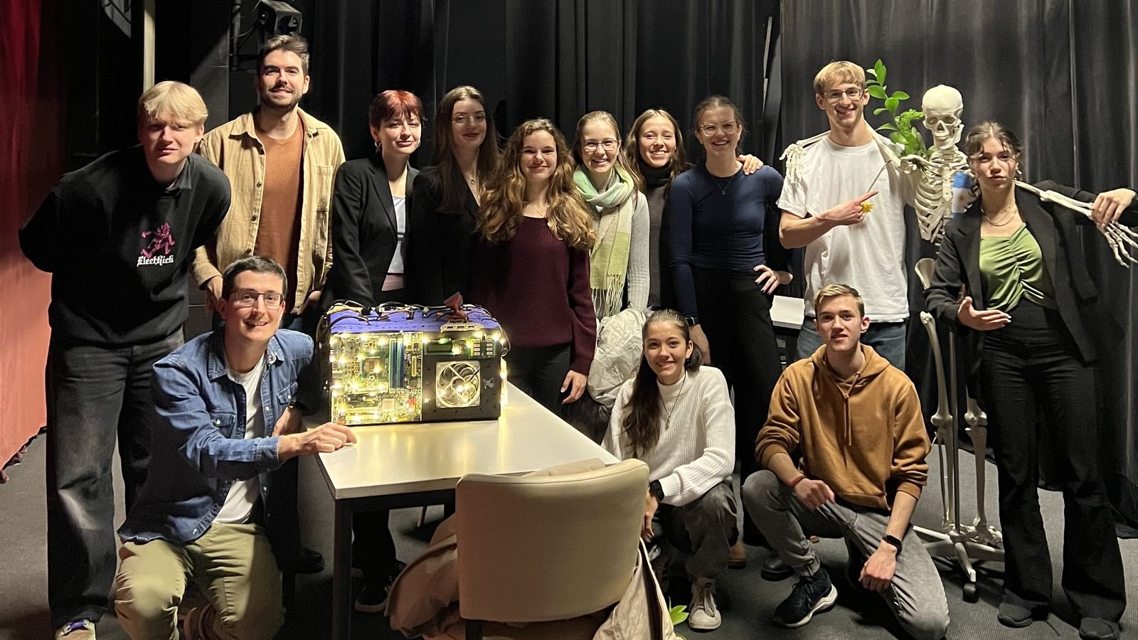El grupo de teatro y sus dos profesores en el escenario, alrededor de la máquina llena de luces y del esqueleto de la clase de ciencias